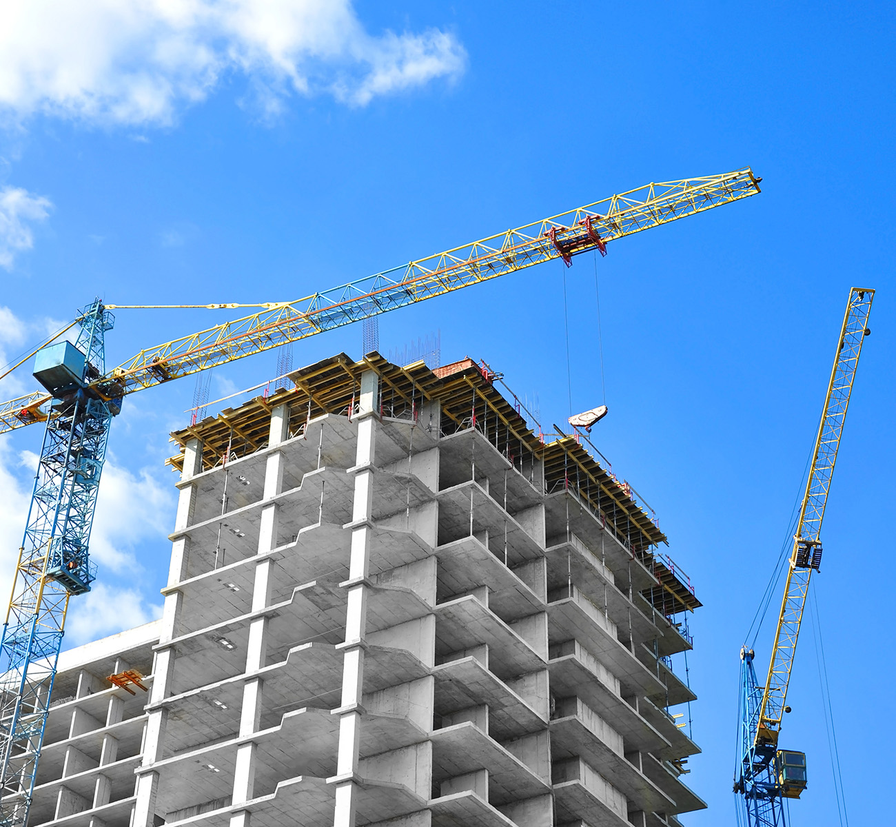 Baukräne über mehrgeschossigem Wohnhaus vor blauem Himmel